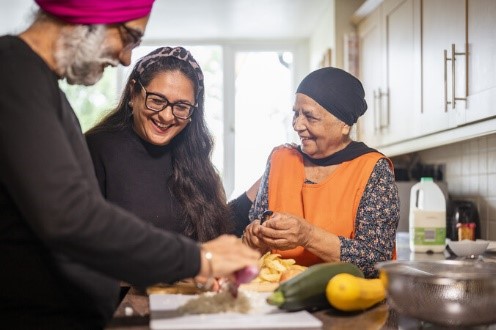 Image of 3 people from different generations preparing food. They are smiling and enjoying each others company